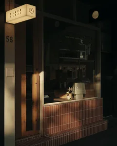 Night view of a modern storefront featuring a warm wooden door, terracotta tile wainscoting, illuminated Black Blaze sign, and a small floral arrangement in the window.