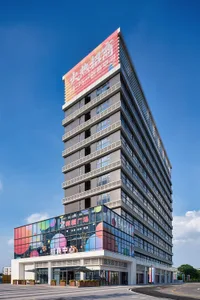 Exterior view of a tall modern office building with a colorful glass facade on the lower levels and large Chinese signage, set against a clear blue sky.