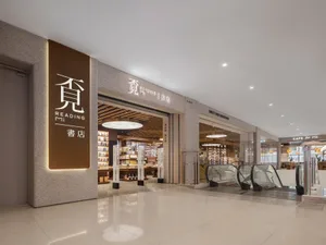 Modern bookstore entrance featuring a large illuminated brown sign with Chinese characters for Reading Mi, textured terrazzo walls, polished reflective floor, and escalators visible in the background of a spacious shopping mall.