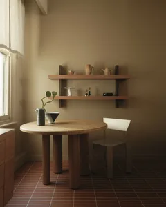 極簡用餐角落，包含實心橡木圓形基座餐桌、現代軟墊椅、展示陶瓷的懸浮木架，以及窗邊的赤陶地磚與亞麻窗簾。