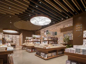 Modern bookstore interior with extensive wooden slat ceiling, large circular pendant lights casting leaf patterns, and bookshelves filled with books.