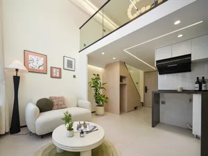 Modern double-height living room with white sofa, round coffee table, light wood cabinetry, marble kitchen island, and glass railing on the upper floor.