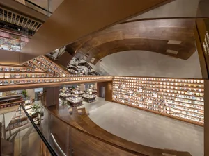 High-angle view of a spacious multi-level bookstore interior featuring extensive curved wooden bookshelves, warm lighting, and an open atrium with glass railings.