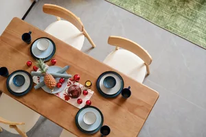 俯視實木長方形餐桌，桌上擺放藍白陶瓷餐具、白色坐墊木椅，以及以鳳梨為主體的聖誕節慶布置與紅色小球。