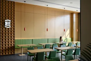 Modern restaurant interior with green leather booths, matching green chairs, light wood tables, and a prominent wooden lattice feature wall with hanging red pendant lights.