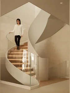 Woman descending a modern sculptural spiral staircase with integrated LED lighting, glass railing, and travertine stone walls in a minimalist luxury interior.