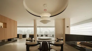 Modern luxury dining room featuring a large round white marble table, four upholstered dining chairs with dark wood frames, and a dramatic three-tiered white pendant light hanging from a curved ceiling detail.