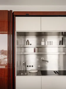 Modern kitchen featuring rich walnut wood cabinetry on the left and a brushed stainless steel open shelving unit with minimalist countertop and induction cooktop.