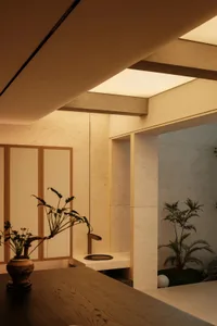 Modern Japanese minimalist interior featuring a small indoor courtyard with travertine stone walls, wooden bonsai planter, and integrated water feature under soft warm lighting.