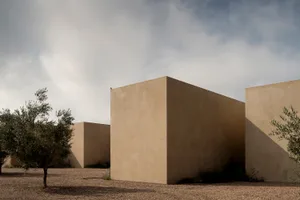 Modern minimalist rammed earth architectural volumes in a desert landscape with olive trees and dramatic cloudy sky