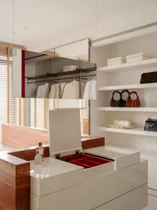 Modern luxury walk-in closet with white lacquered cabinetry, onyx marble island, open red-lined drawer, and white open shelving displaying designer handbags.