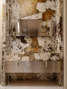 Modern bathroom featuring a double vanity carved from Calacatta marble with bold bronze and brown veining, paired with a floating stainless steel cabinet and a large frameless mirror.