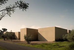 Modern minimalist rammed earth courtyard houses with clean geometric forms surrounded by olive trees and native vegetation under a clear sky at golden hour.
