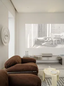 Modern minimalist living room with chocolate brown boucle sofas, cream side table, stainless steel media console, and a large concrete architectural projection on the wall.