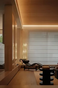 Modern minimalist reading nook featuring a black leather chaise lounge, sculptural paper floor lamp, travertine walls, and warm cove lighting.