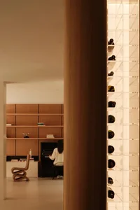 View into a minimalist music room featuring walnut wood shelving, a black upright piano, a sculptural wooden chair, and an illuminated acrylic wine storage wall.