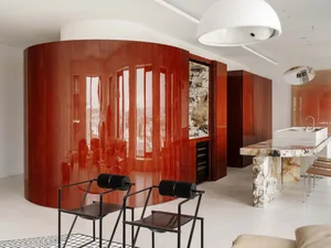 Modern open kitchen featuring a large curved wall of glossy reddish-brown burl wood cabinetry, a Calacatta Viola marble kitchen island with integrated sink, two black metal dining chairs in the foreground, and white spherical pendant lights.