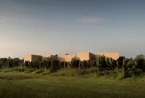 Modern rammed earth vineyard estate building with clean geometric forms surrounded by vineyards in a rural landscape at dusk