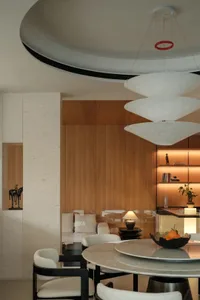 Modern luxury dining room featuring a round travertine marble table, black-framed upholstered chairs, curved ceiling detail, and warm wooden built-in cabinetry with integrated lighting.