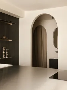 Modern minimalist interior featuring dramatic arched passageways, dark wood built-in cabinetry with floating shelves, metallic decorative objects, and a neutral color palette.