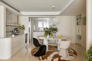 Modern dining area featuring a round Calacatta marble table, black Panton chair, cream boucle chairs, and a brown-and-white cowhide rug in a bright open-plan kitchen and living space.