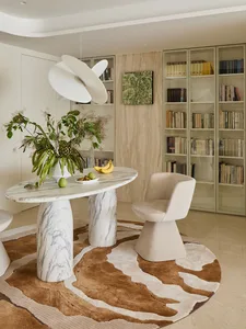 Modern dining area featuring a round Calacatta marble table on sculptural bases, a cream bouclé swivel chair, a large white pendant lamp, and floor-to-ceiling built-in bookshelves with light wood paneling.