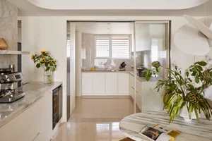 Modern open-concept kitchen with white cabinetry, Calacatta marble countertops and island, stainless steel espresso machine, and large white pendant light.