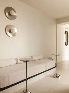 Minimalist living room with a cream boucle daybed, two round marble side tables with chrome bases, and two circular metallic wall sconces with spherical lights.