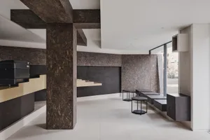 Modern minimalist cafe interior featuring dark marble walls, large structural beams, floating black stone benches and round side tables against a bright white floor.