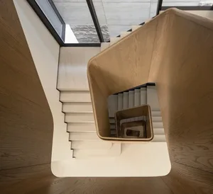 Top-down view of a modern curved oak staircase with continuous wooden handrail and floating light-colored steps in a minimalist interior.