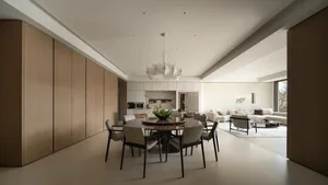 Modern minimalist dining room featuring a round dark marble table, six light grey upholstered chairs, a large white sculptural chandelier, and full-height oak cabinetry that flows into an open living room in the background.