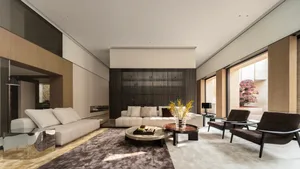 Modern luxury living room featuring a tall walnut slatted accent wall, creamy white sectional sofa, dark brown leather armchairs, round marble coffee tables, and a large abstract area rug under bright natural light from floor-to-ceiling windows.