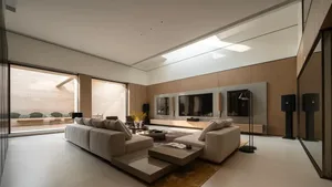 Modern minimalist living room featuring a large L-shaped beige sectional sofa, low wooden coffee table, oak wall paneling, large wall-mounted TV, and a long skylight allowing abundant natural light.