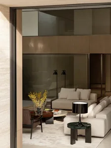 Modern luxury living room featuring a large beige sectional sofa, matching armchair, round coffee tables, black floor lamps, and warm wood paneling in the background.