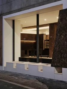 Night view of a modern minimalist cafe with white marble stepped seating and dark brown marble interior walls visible through large glass windows.