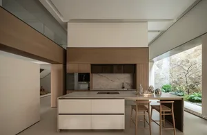 Modern minimalist kitchen featuring a large marble island with wooden bar stools, integrated wood cabinetry, and a large window overlooking a rock garden.