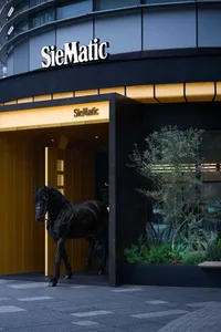 Modern luxury storefront with black marble facade, golden backlit entrance, a realistic black horse sculpture, and landscaped greenery.