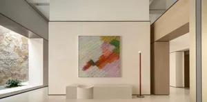 Modern minimalist entryway with large colorful abstract painting, curved concrete bench, wooden floor lamp, and natural stone garden view.