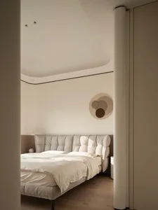 Modern minimalist bedroom with a large tufted boucle fabric bed, white bedding, round woven wall art, and curved ceiling details in neutral tones.