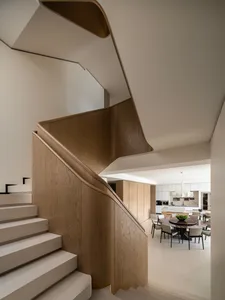 Modern interior view of a curved oak staircase with white risers overlooking a dining area featuring a round marble table and pendant lights.