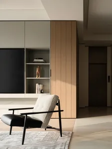 Modern living room featuring a black and white boucle armchair with black metal frame on a textured rug, positioned in front of built-in light wood and off-white cabinetry with open shelving and a large television.