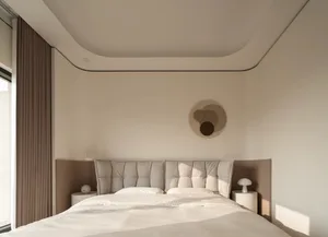 Minimalist bedroom with a large tufted light-grey fabric headboard, white bedding, curved ceiling detail, and neutral beige walls.