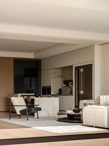 Modern minimalist living room featuring a white marble kitchen island, boucle sofa, black leather and wood armchair, and integrated stainless steel appliances.