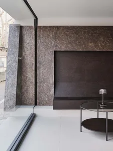 Modern minimalist living room featuring a large raw oriented strand board feature wall, concrete-like pillar, round glass coffee table, and a modern table lamp.