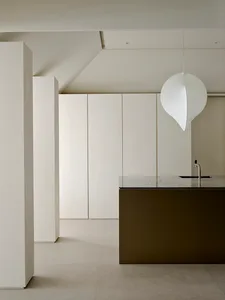 Modern minimalist kitchen featuring a dark concrete island, white seamless cabinetry, and a large white sculptural pendant lamp hanging above.