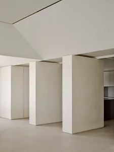 Minimalist living room interior featuring off-white micro-cement walls, a floating partition wall, high ceilings with recessed lighting, and seamless concrete flooring.