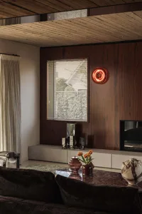 Modern living room featuring dark walnut wood paneling, a marble coffee table with glass and ceramic decor, a concrete media console, and warm ambient lighting from a red neon wall sconce.