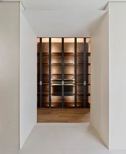 Modern minimalist walk-in closet featuring dark metal framed glass doors and backlit walnut wood open shelving with warm lighting.