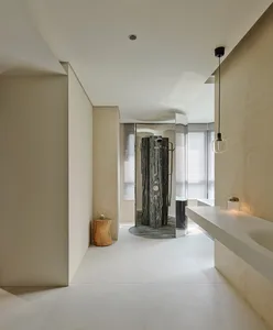 Modern minimalist bathroom with beige textured walls, white floor tiles, a dramatic dark marble open shower, floating white vanity, and a natural wood stump stool.