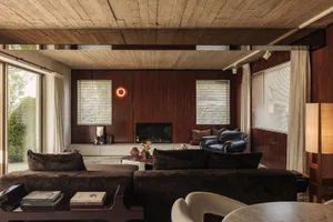 Mid-century modern living room with dark walnut wood paneling, brown velvet sectional sofa, leather lounge chairs, and a wooden ceiling.
